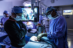 Sunil Singhal, MD, examines lung tissue during a surgical procedure using a glowing tumor agent, while a colleague observes.